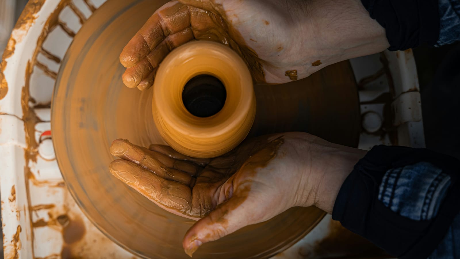 Manos de un artesano modelando arcilla bajo la luz del taller